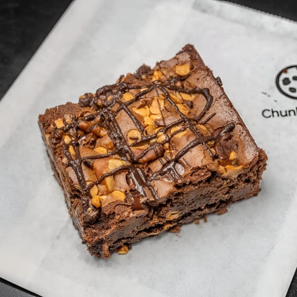 A Chunky Bites brownie with chocolate drizzle and peanut butter chips on white parchment paper.