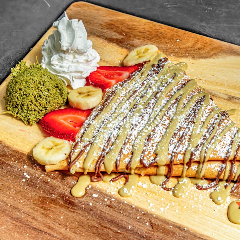 Chunky Bites' crepe with chocolate and pistachio drizzle, powdered sugar, strawberries, bananas, and whipped cream.