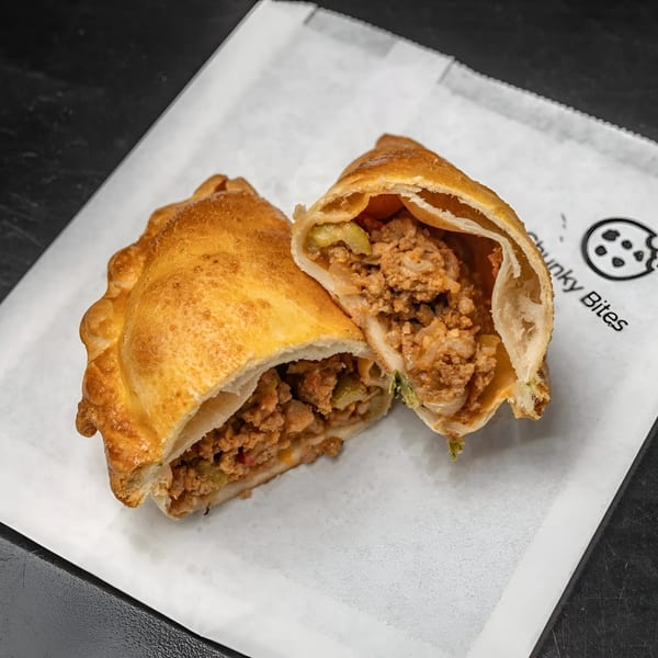 A golden-brown empanada from Chunky Bites, sliced open to reveal a savory meat and vegetable filling.